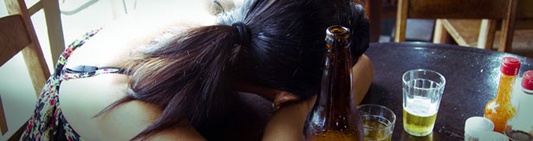 Foto de uma mulher dormindo em uma mesa com uma garrafa de cerveja do lado