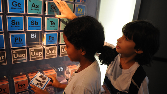 Um menino e uma menina brincam com tabela periódica interativa