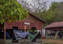 Duas casas da aldeia indígena Yanomami em Roraima. O chão é de terra é o local cercado por árvores baixas.