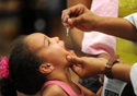Foto de uma menina tomando vacina em gota