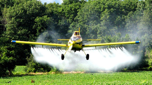 Avião pequeno lançando nuvem de agrotóxico sobre plantação