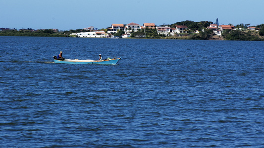 Barco com dois pescadores atravessando um rio, com uma cidade ao fundo