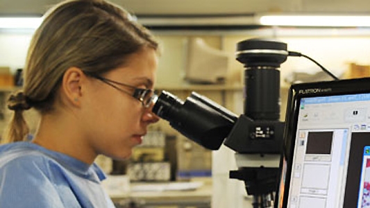 Jovem em laboratório observa ao microscópio 