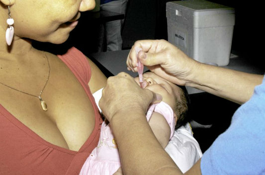 Bebê no colo da mãe tomando vacina em gotas