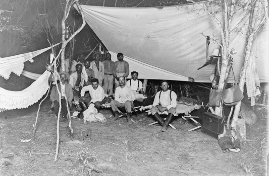 Foto antiga mostra homens sentados embaixo de uma tenda
