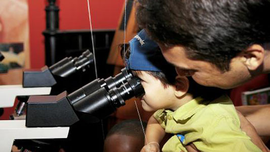 Criança usa o microscópio com auxílio de um adulto 