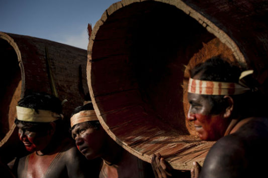 Close de índios carregando troncos de madeira em ritual