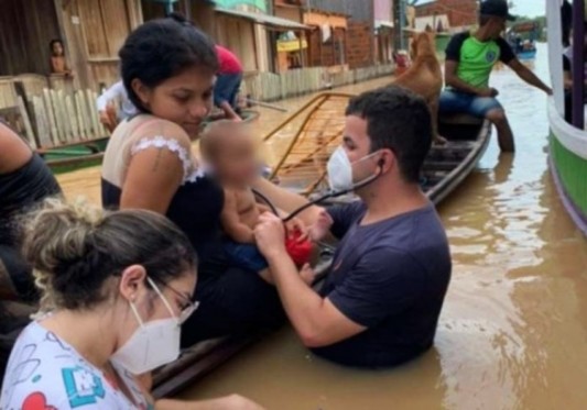 Médico no Acre atendendo uma criança que está dentro de uma canoa com a água na cintura