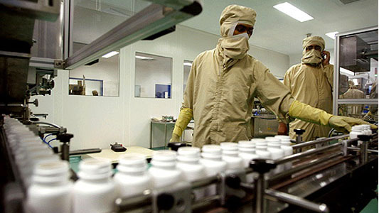 Funcionários operam equipamento com série de frascos de remédios