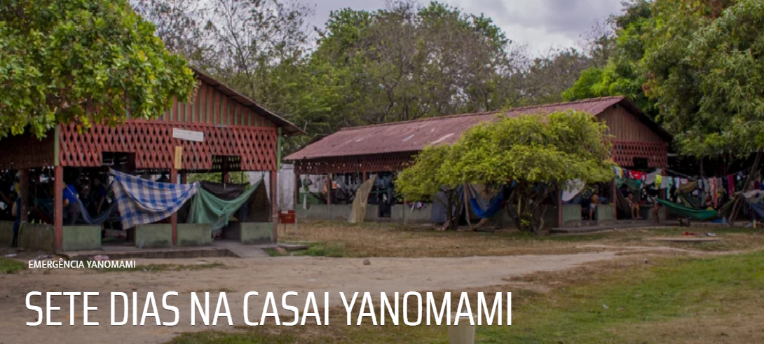Duas casas da aldeia indígena Yanomami em Roraima. O chão é de terra é o local cercado por árvores baixas.
