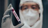 Técnico de laboratório em traje de EPI segurando amostra de sangue contendo Covid-19