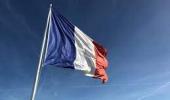Imagem com fundo azul, a frente a bandeira da França, nas cores azul, branco e vermelho em listras verticais