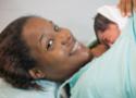 Mulher sorri com bebê recém-nascido sobre o seio