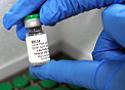 Close na mão de um pesquisador, de luvas, mostra um frasco da vacina
