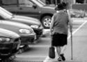 De costas, mulher idosa caminha por um estacionamento