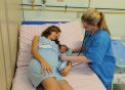 Mulher com bebê recém-nascido ao lado em uma maca recebe atenção outra mulher profissional de saúde