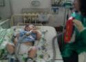 Um bebê, deitado num leito hospitalar, presta atenção numa educadora com um equipamento na mão