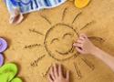 Foto de uma criança desenhando o sol na areia